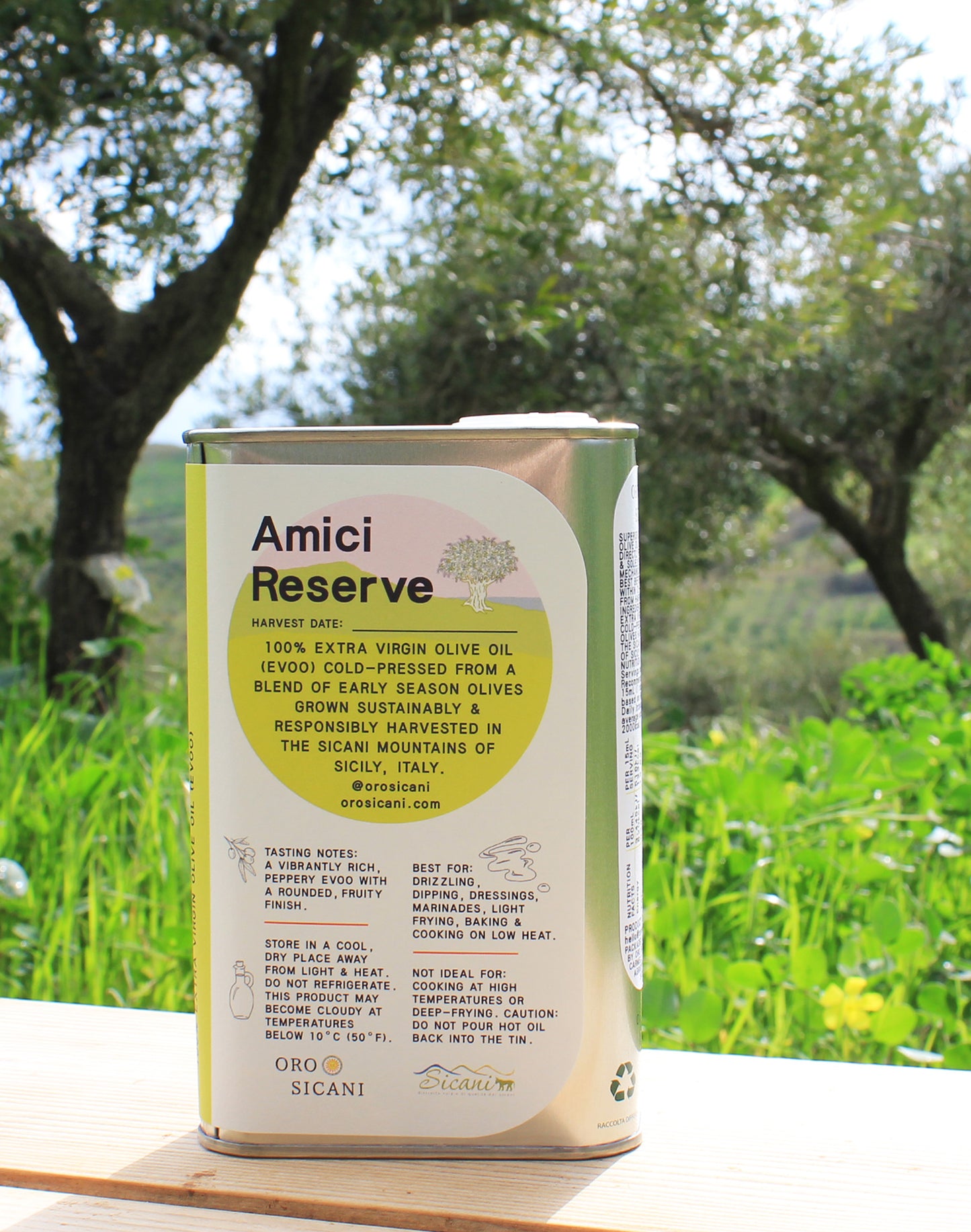 Close-up of ORO SICANI Amici Reserve 100% Extra Virgin Olive Oil tin on top of wooden table with olive trees on ORO SICANI Estate in the background.