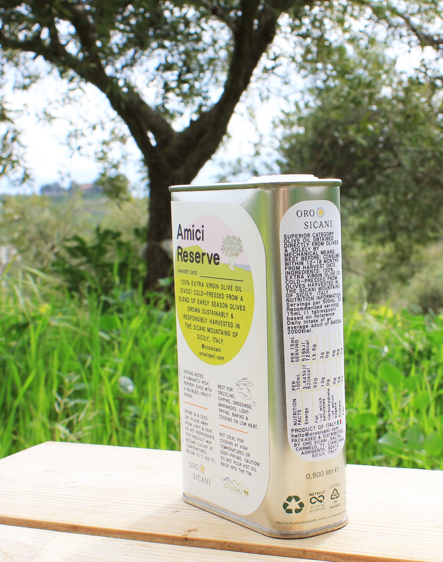 Close-up of ORO SICANI Amici Reserve 100% Extra Virgin Olive Oil tin on top of wooden table with olive trees on ORO SICANI Estate in the background.