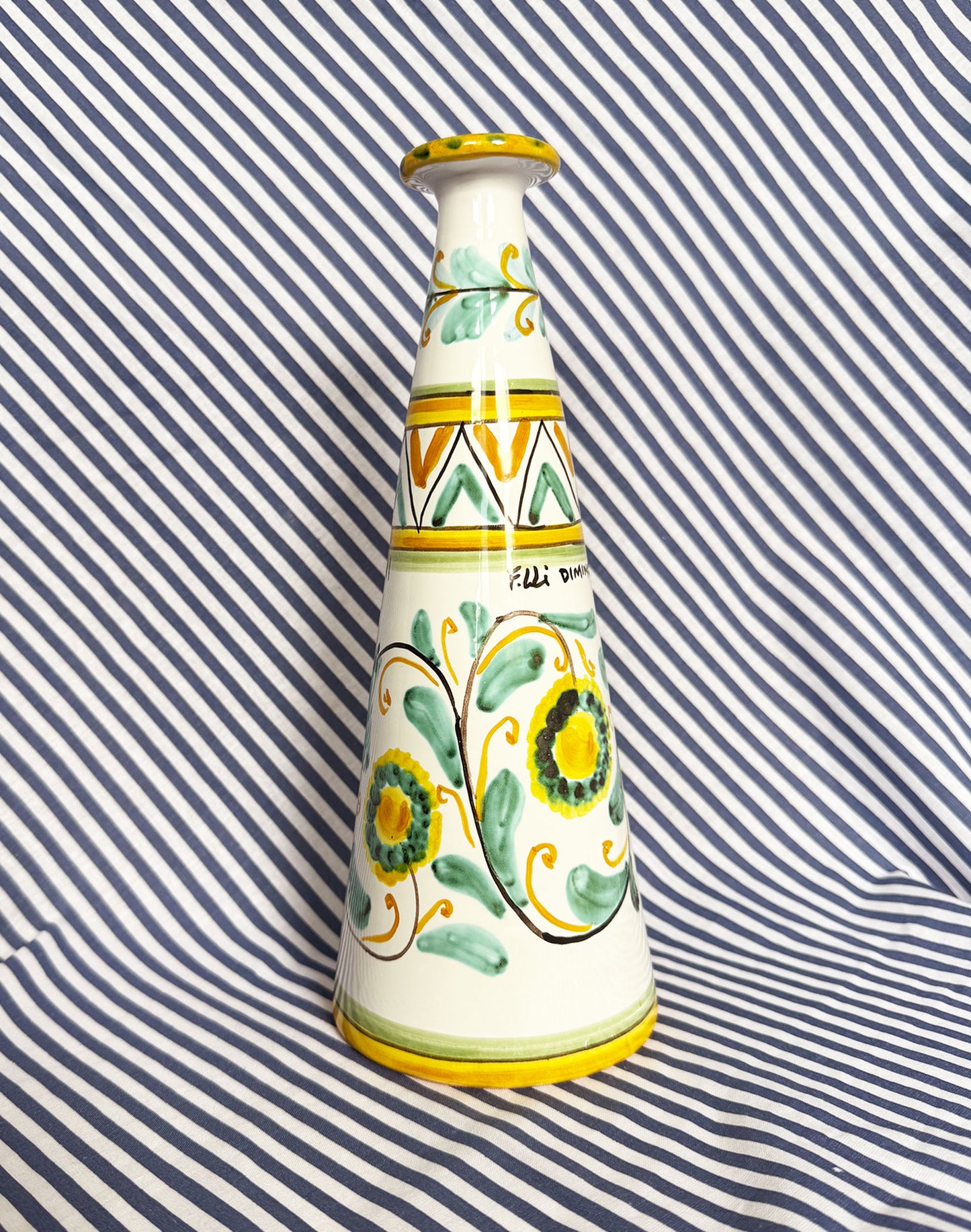 Hand-painted Sicilian ceramic bottle with blue flower patterns in front of a striped background