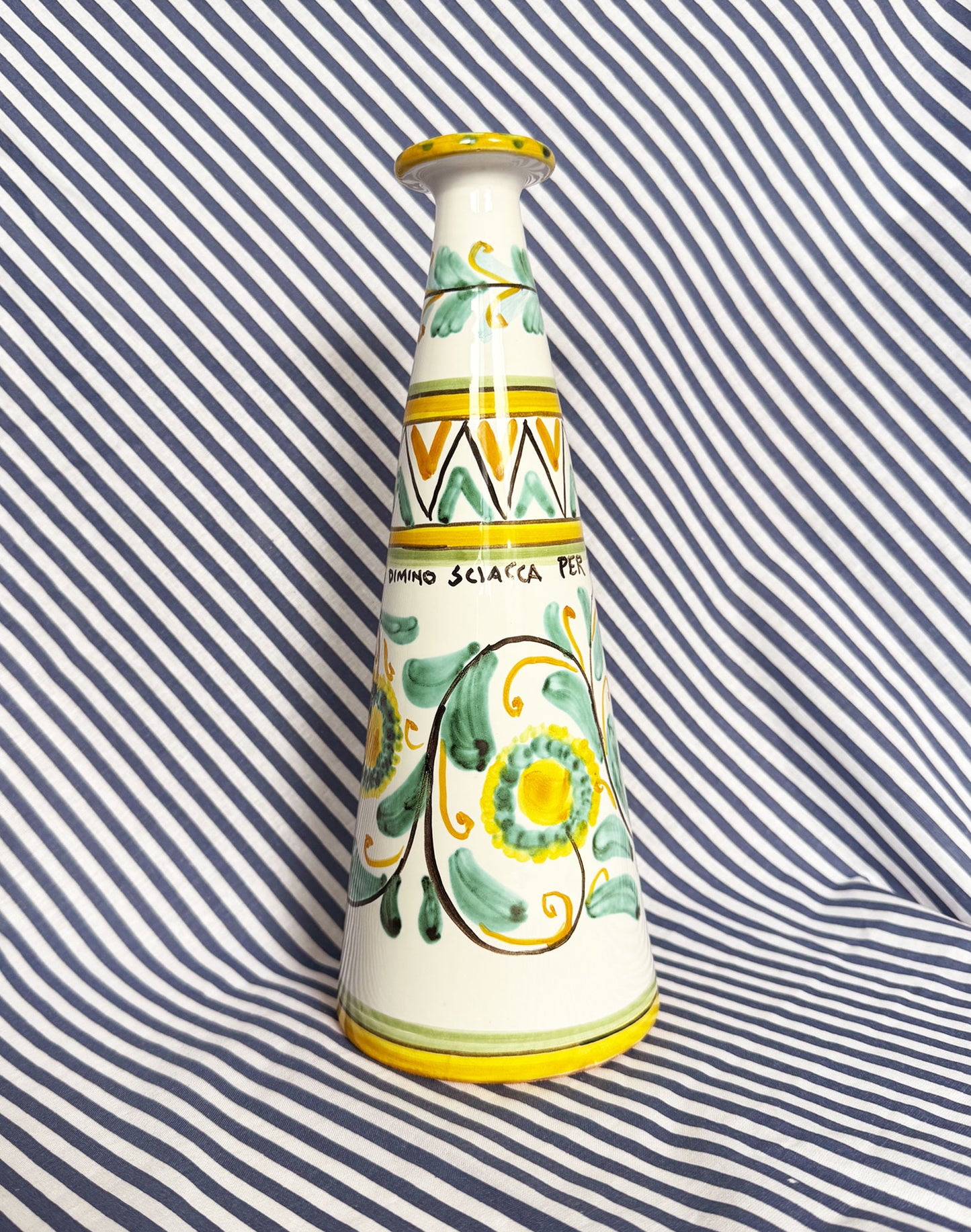 Hand-painted Sicilian ceramic bottle with blue flower patterns in front of a striped background