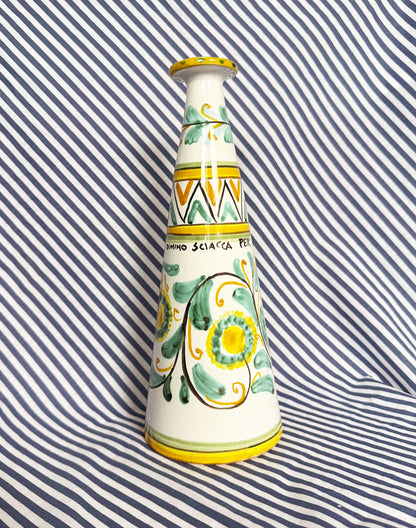 Hand-painted Sicilian ceramic bottle with blue flower patterns in front of a striped background