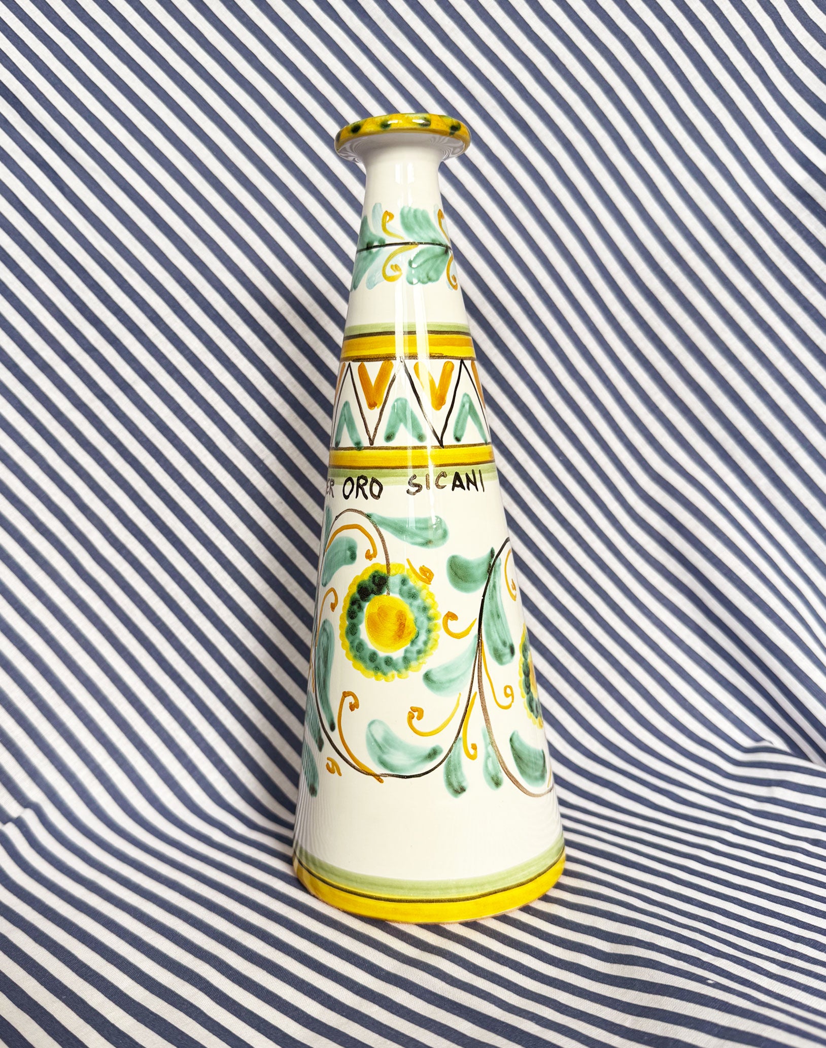 Hand-painted Sicilian ceramic bottle with blue flower patterns in front of a striped background