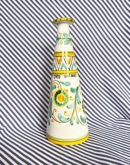 Hand-painted Sicilian ceramic bottle with blue flower patterns in front of a striped background