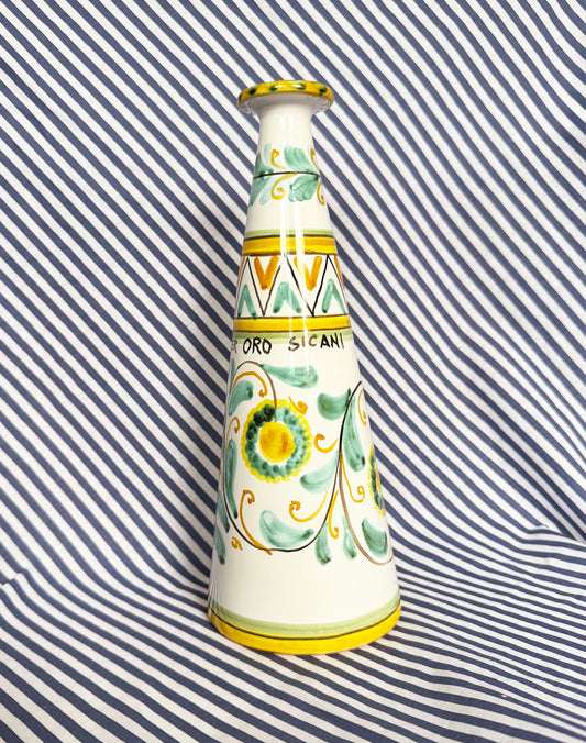 Hand-painted Sicilian ceramic bottle with blue flower patterns in front of a striped background