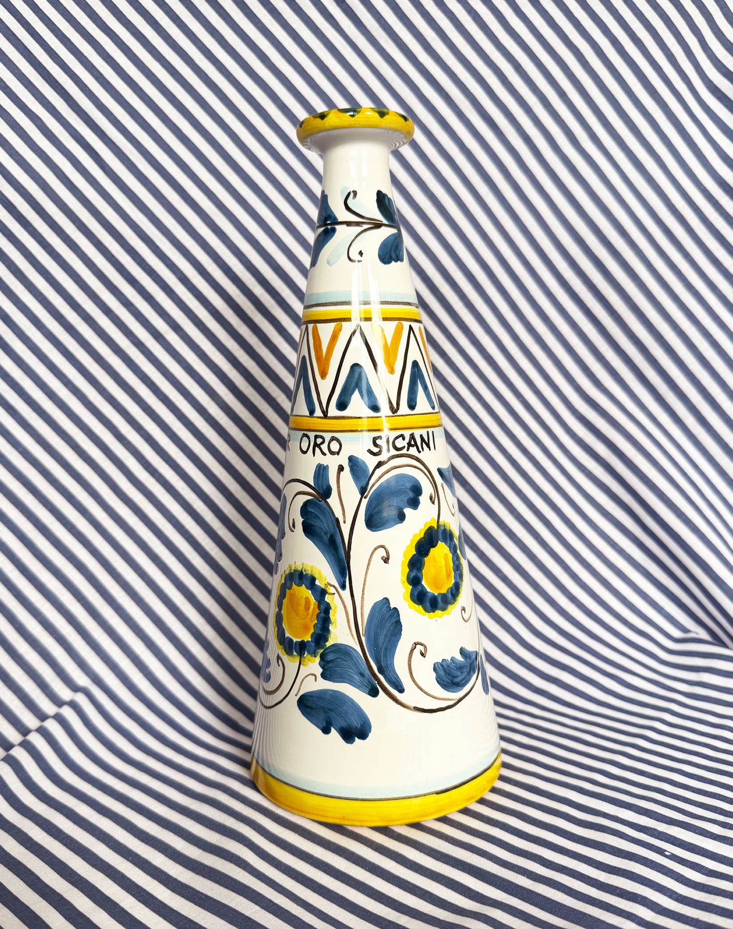 Hand-painted Sicilian ceramic bottle with blue flower patterns in front of a striped background