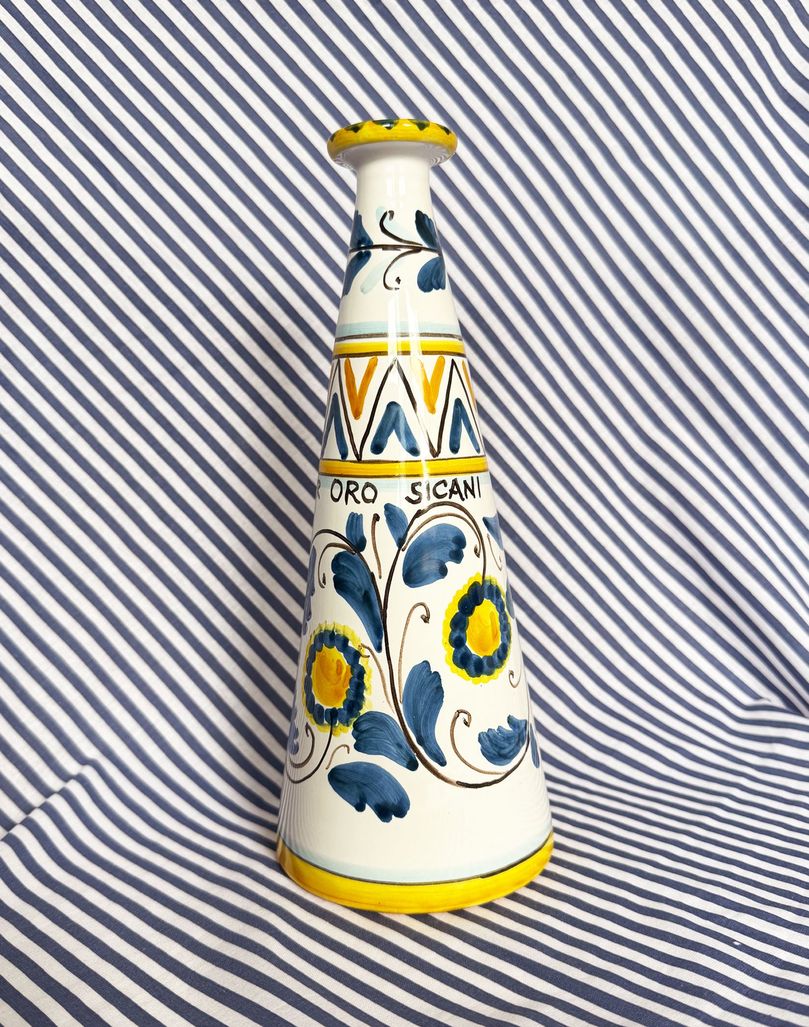 Hand-painted Sicilian ceramic bottle with blue flower patterns in front of a striped background