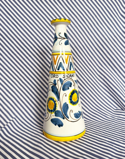 Hand-painted Sicilian ceramic bottle with blue flower patterns in front of a striped background