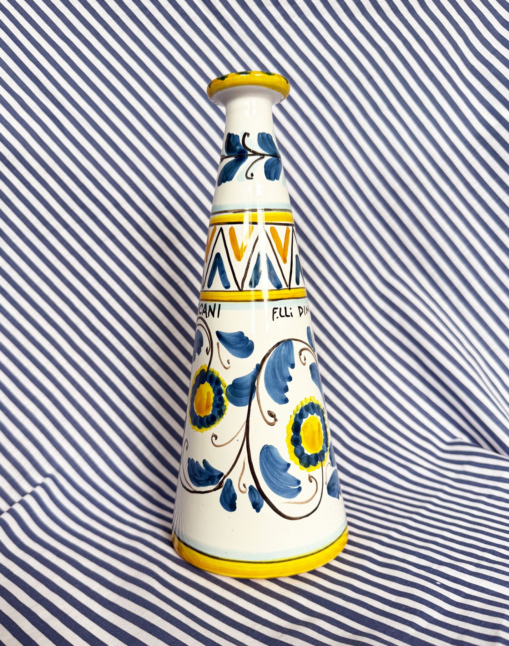 Hand-painted Sicilian ceramic bottle with blue flower patterns in front of a striped background