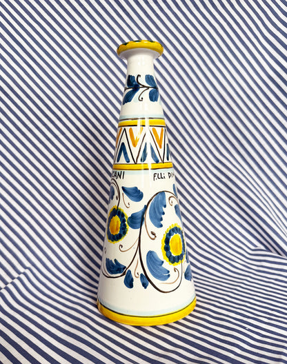 Hand-painted Sicilian ceramic bottle with blue flower patterns in front of a striped background