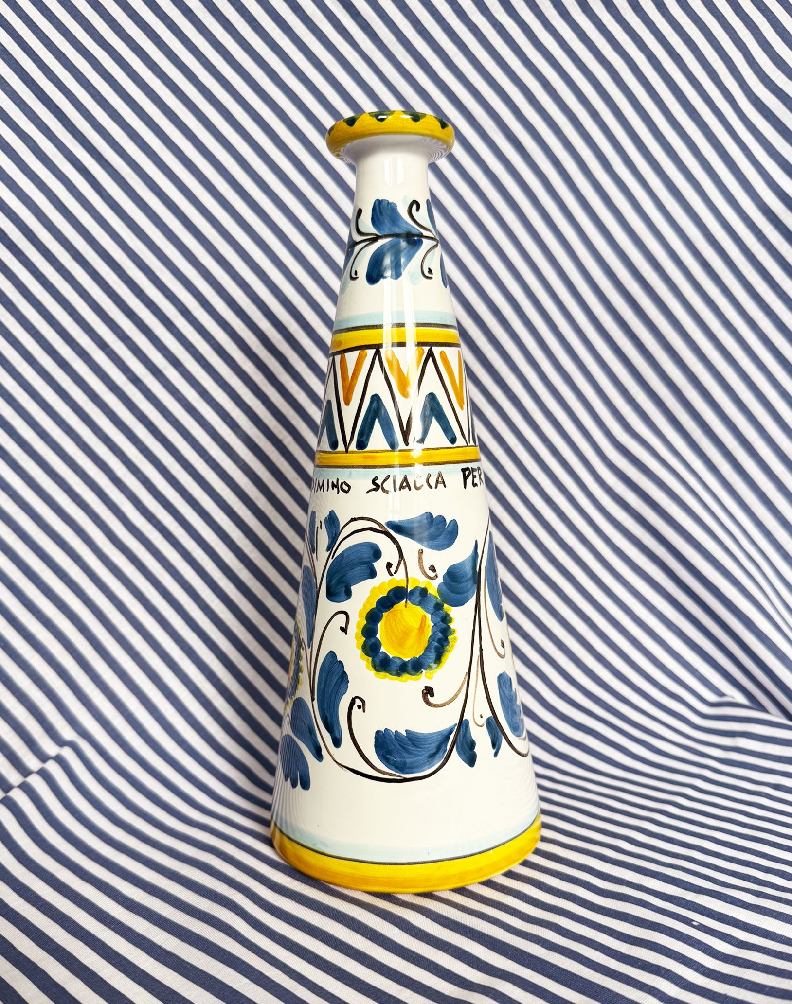 Hand-painted Sicilian ceramic bottle with blue flower patterns in front of a striped background