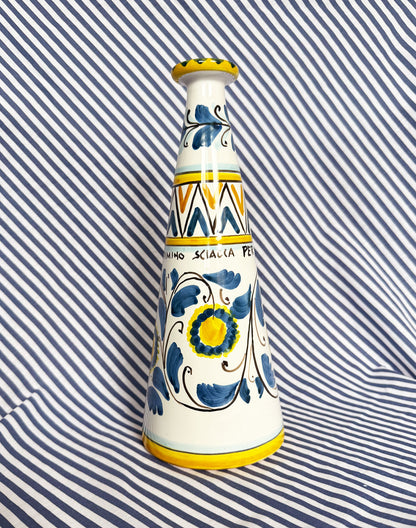 Hand-painted Sicilian ceramic bottle with blue flower patterns in front of a striped background