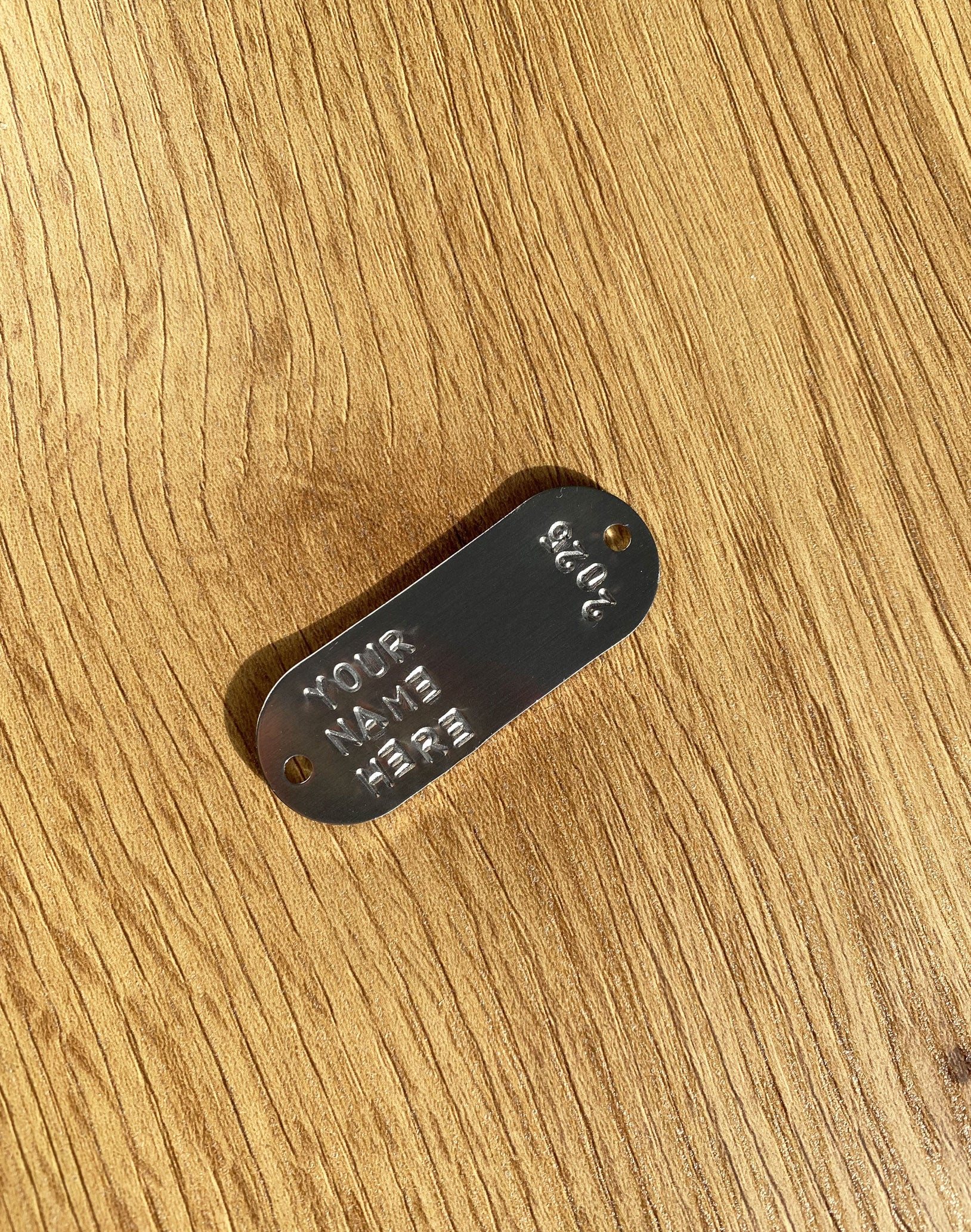 Metal tag with 'Your Name Here' text on a wooden surface