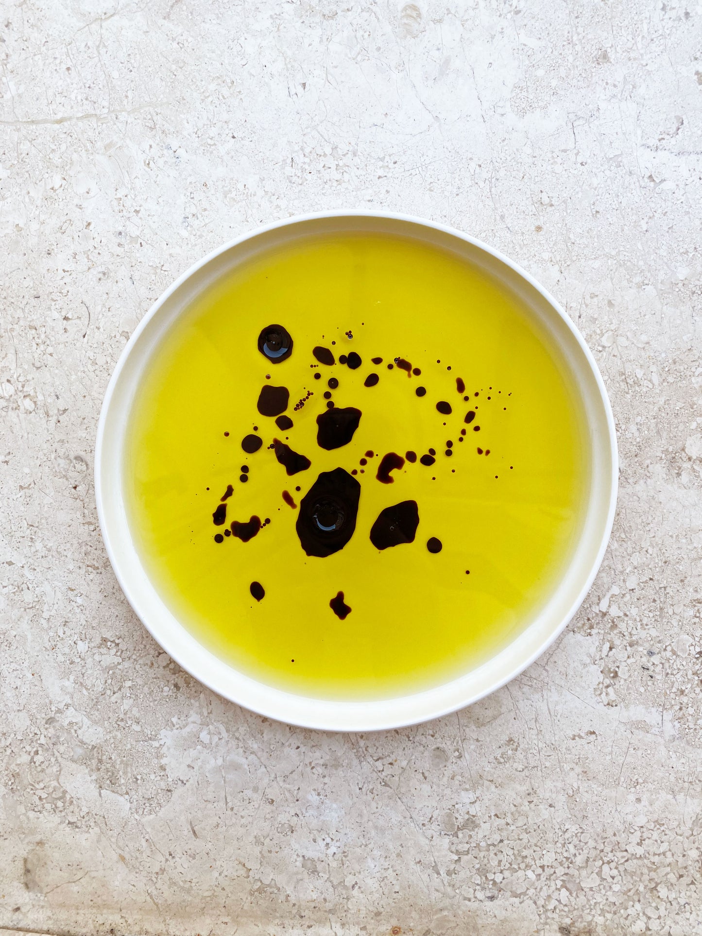 White dish with oro sicani sicilian extra virgin olive oil and balsamic vinegar on travertine marble tabletop