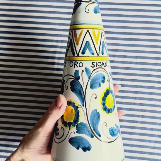 360 degree view of hand-painted Sicilian ceramic bottle with blue flower patterns in front of a striped background