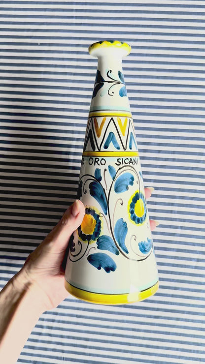 360 degree view of hand-painted Sicilian ceramic bottle with blue flower patterns in front of a striped background
