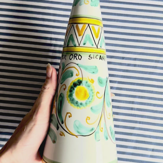 360 degree video of hand-painted Sicilian ceramic bottle with blue flower patterns in front of a striped background