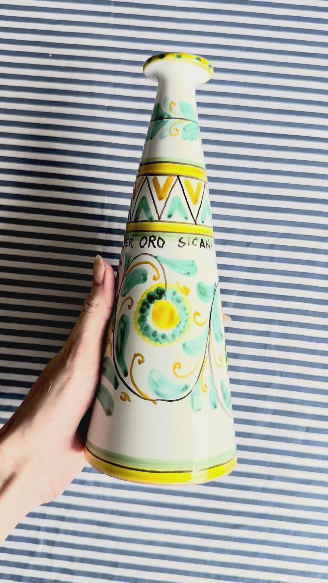 360 degree video of hand-painted Sicilian ceramic bottle with blue flower patterns in front of a striped background